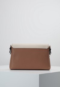 Brown and cream leather clutch with a textured surface, zip closure, and decorative tassels on the sides. Rectangular shape.