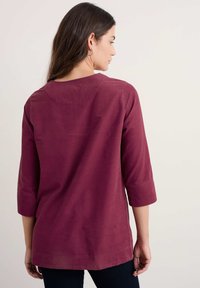 Bordo krekls ar trim ceturtdaļu piedurknēm, apaļu izgriezumu un gludu tekstūru. Piedāvā vienkāršu dizainu, kas krīt līdz vidukļa vidum.