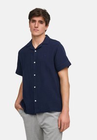 Camisa de botones de manga corta en color azul marino, hecha de tejido texturizado, con un bolsillo, cuello tipo campamento y botones blancos.