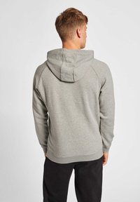Grå hoodie med tekstureret overflade, der har en snoretrækshætte og ribbede manchetter. Designet inkluderer raglanærmer og en afslappet pasform.