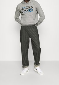 Felpa grigia con logo "JACK&JONES" in blu e nero, abbinata a pantaloni a righe scure e sneakers Nike bianche con dettagli neri.