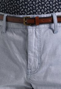 Jasnoniebieskie spodnie z mieszanki bawełny o gładkiej fakturze, wyposażone w brązowy skórzany pasek oraz subtelne skośne przeszycia na kieszeniach.
