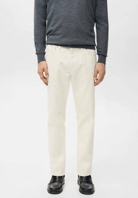 Pantalones de algodón blanco con diseño de pierna recta, combinados con un suéter de manga larga gris oscuro y zapatos negros. Acabado simple y limpio.