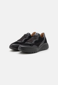 Black athletic shoes with a mix of suede and leather, featuring a rounded toe, thick sole, and black laces, providing a textured look.