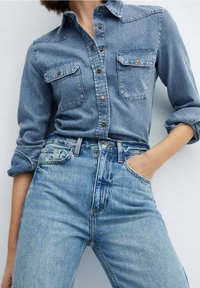 Chemise en jean avec deux poches poitrine et devant boutonné, associée à un jean taille haute bleu clair. Les deux pièces présentent une coupe classique et décontractée.