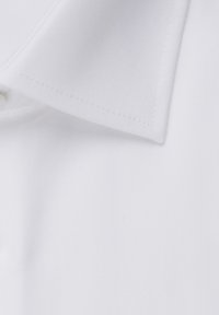 Gros plan sur le col d'une chemise blanche propre et nette avec des coutures visibles sur un tissu lisse.