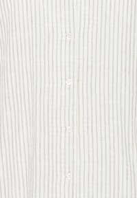 Gros plan d'une chemise blanche avec de fines rayures verticales beiges et des boutons blancs au centre.