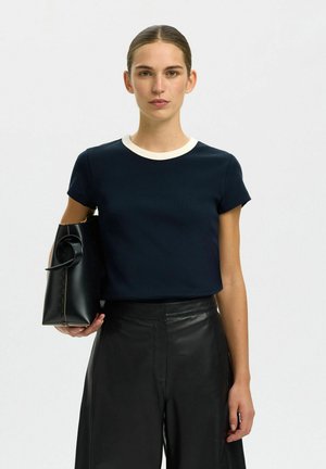 Nāvijstas zilas īsām piedurknēm T-krekls ar kontrastējošu krēmkrāsas ribotu apkakli, kombinēts ar melnām augstas jostasvietas ādas biksēm un melnu rokassomu.