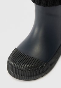 Μπλε καουτσούκ μπότες με ribbed μαύρη καουτσούκ προστασία στα δάχτυλα και πλεκτό κρόσσι στην κορυφή. Λείο επιφάνεια και στρογγυλό σχήμα.