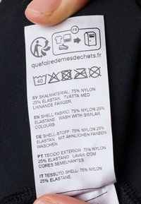 Etichetta di cura dei tessuti su tessuto nero, che mostra le istruzioni di lavaggio e la composizione del materiale: 75% nylon, 25% elastan, in più lingue.
