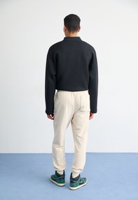 Černý pulovr s pohodlným střihem a límečkem, doplněný krémovými tepláky. Stylizováno s zeleno-černými teniskami. Hladká textura a jednoduchý design.