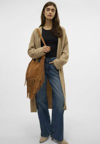 Beige Strickjacke, schwarzes Top, weitgeschnittene Denim-Jeans und eine braune Wildleder-Fransenhandtasche mit langen Quasten. Schuhe mit Absatz in neutralen Tönen.