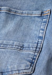 Tela de mezclilla azul con un bolsillo trasero con costuras naranjas. La tela tiene un acabado texturizado con un ligero brillo y patrones de tejido visibles.