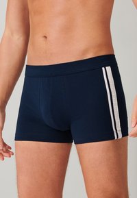 Bóxer azul marino fabricado con tejido elástico, que presenta rayas verticales blancas en los lados y una cómoda cintura elástica.