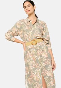 Abito camicia verde chiaro con motivo floreale in rosa e beige. Presenta maniche lunghe, uno spacco laterale e una cintura intrecciata con una fibbia circolare.