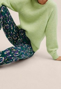 Jasnozielony, teksturowany sweter w połączeniu z wzorzystymi niebiesko-zielonymi spodniami z purpurowo-kremowymi wzorami, siedzący na neutralnym tle.
