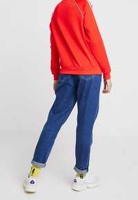 Červená mikina s bílým lemem, modré zužující se džíny s ohrnutými lemy a bílé tenisky se žlutými ponožkami. Neformální sportovní oblečení.