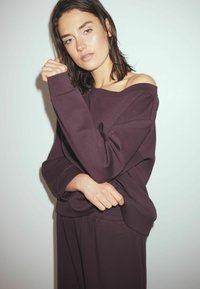 Burgundi värvi üle mõõtmete dressipluus, millel on avatud õlavarre disain, tekstuurne kangas ja elastsed mansetid, koos vastava hõlmikuga. Lihtne, moodne stiil.