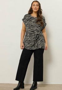 Top de estampado en blanco y negro con mangas cortas y detalle de torsión, combinado con pantalones anchos de tiro alto en negro y botas de tobillo negras.