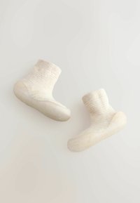 Gestrickte cremefarbene Socken mit einem strukturierten Muster, elastischem Bündchen und glatten, einfarbigen Gummisohlen, die für Komfort und Flexibilität konzipiert sind.