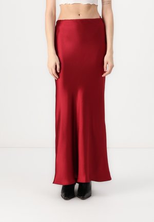 Długa, dopasowana spódnica z satyny w głębokim czerwonym kolorze. Gładka faktura z subtelnym połyskiem. Dół sięga do podłogi. Połączona z czarnymi botkami za kostkę.