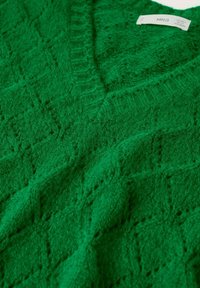 Sweater vert tricoté avec un motif en losanges et un col en V, présentant une étiquette de marque blanche visible sur le côté supérieur droit.