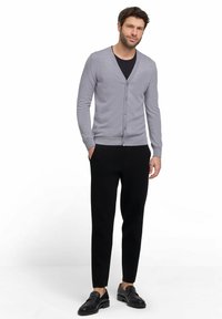 Cardigan grigio chiaro con scollatura a V, chiusura a bottoni, polsini e orlo a coste, abbinato a pantaloni neri slim-fit e mocassini neri.
