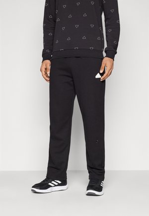 Sweatshirt noir avec des motifs triangulaires blancs et pantalon de survêtement noir. Le pantalon de survêtement présente un logo accentué sur le côté gauche. Porté avec des chaussures de sport noires.
