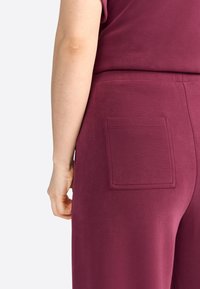 Burgunderfarbene Hosen mit einer glatten, strukturierten Oberfläche. Verfügt über eine quadratische Gesäßtasche mit verstärkten Nähten. Einfaches Design, lässiger Stil.