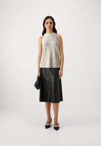 Light gray sleeveless top with a textured finish, paired with a black leather skirt. Model holds a small black handbag, wearing black heels.