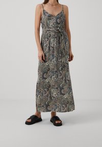 Robe maxi avec un motif cachemire dans des couleurs pastel. Dotée de fines bretelles et d'une taille à lien. Associée à des sandales à glisser noires. Texture de tissu lisse.