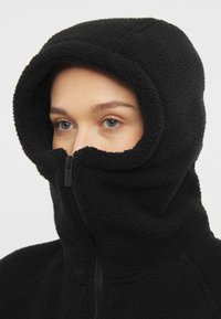 Felpa nera in pile con colletto alto e zip a tutta lunghezza. Texture morbida con un design aderente e un cappuccio oversize.