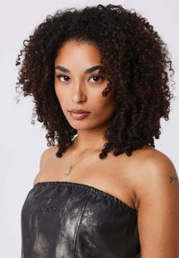Black, strapless top made of shiny fabric with a gathered neckline, worn by a person with curly hair, featuring a gold necklace and arm tattoo.