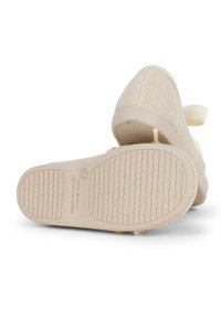 Beige textile shoes with woven upper, light rubber sole, and a textured pattern on the bottom. Adjustable strap for secure fit.