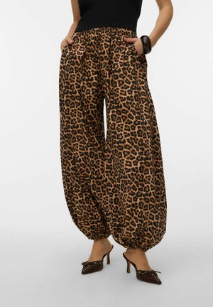 Femme portant un pantalon à jambes larges imprimé léopard avec chevilles froncées, un haut noir sans manches, un bracelet marron et des chaussures marron à talons hauts.