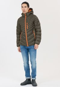 Olivengrøn pufferjakke med hætte, med orange lynlåse, struktureret chevronmønster og sidelommer. Parret med blå jeans og sorte støvler.