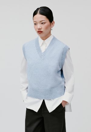 Gilet tricoté bleu clair avec un col en V et un ourlet côtelé, porté sur une chemise blanche à col. Texture lisse, sans manches.