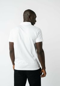 Weißes Poloshirt mit Kragen und kurzen Ärmeln, aus Baumwolle, mit einem schlichten Design und weicher Textur, kombiniert mit dunklen Hosen.