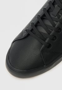 Μαύρο δερμάτινο αθλητικό παπούτσι με υφή, σχέδιο με κορδόνια, διακριτές ραφές και καουτσούκ σόλα. Κοντινή άποψη της περιοχής των δακτύλων.