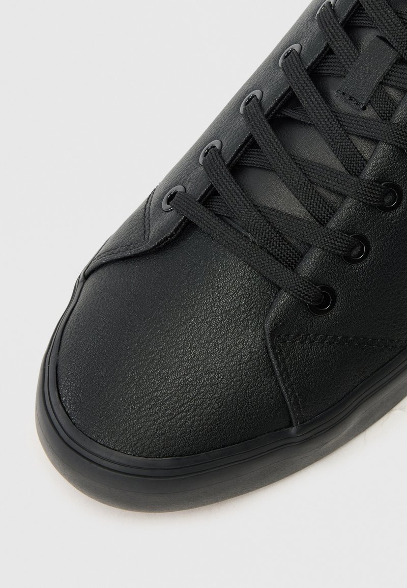 Zwarte leren sneaker met een textuur, vetersluiting, subtiele stikdetails en een rubberen zool. Close-up van het teengebied.