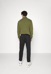 Olivgrön tröja med hög krage, i kombination med svarta sweatpants. Grå och vita sportskor med neongula detaljer.