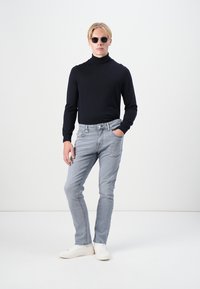 Schwarzer Rollkragenpullover, hellgraue Slim-Fit-Jeans und weiße Sneaker. Runde Sonnenbrille vervollständigt das Outfit. Glatte Textur, moderner Schnitt.
