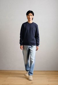 Sweatshirt azul-marinho com decote redondo e corte reto, combinado com jeans azul claro e sapatilhas claras. Design simples, sem padrões ou detalhes.