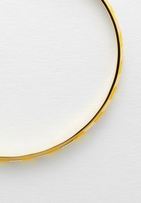 Bracciale d'oro con superficie liscia e accenti gialli testurizzati lungo il bordo, caratterizzato da una forma circolare e un design elegante.