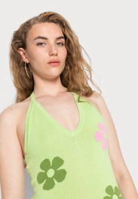 Haut halter tricoté en vert clair avec un décolleté en V, orné de motifs floraux verts et roses. Texture douce avec une coupe décontractée.