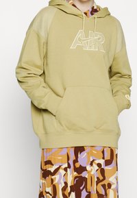 Person wearing a beige Nike Air hoodie with mesh shoulder panels and a multicolored abstract patterned skirt.