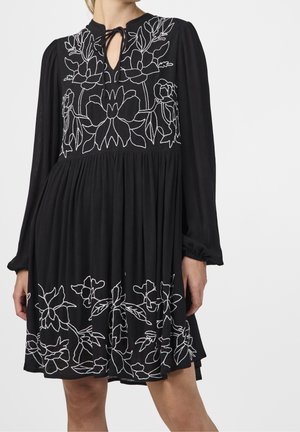 Zwarte jurk met lange mouwen, voorzien van witte bloemenborduursels, een keyhole-halslijn en een geplooide rok. Zachte stof met een gestructureerde afwerking.