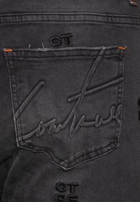 Black denim jeans with stitched logo and details. Features a back pocket with embossed design and orange stitching accents.