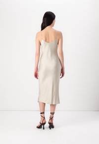 Satin slipklänning i ljus beige med tunna justerbara remmar, rak fåll och slits på sidan. Kombinerad med svarta högklackade sandaler med remmar.