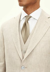 Beige linnekostym med treknappsförslutning, vit skjorta och en strukturerad, ljusgul slips. Passar för formella tillfällen.